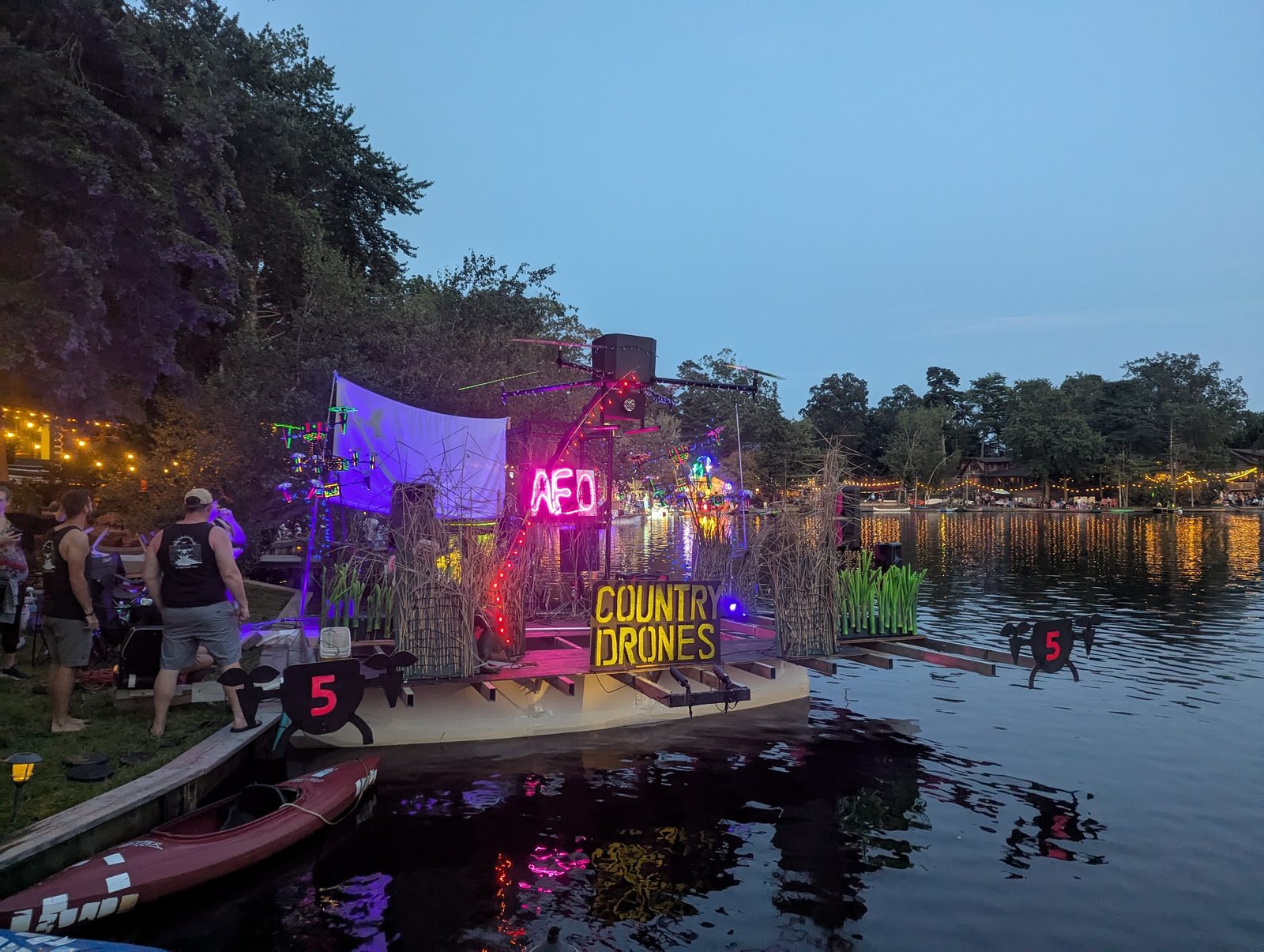Finished float lit up at dusk on the water, Country Drones sign glowing